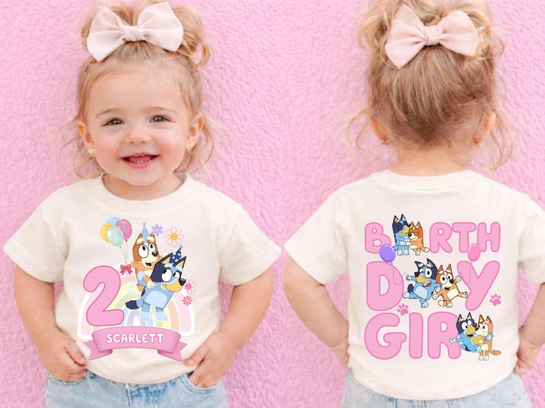 A smiling young girl wearing a white t-shirt with a birthday theme, featuring characters from the children's television show "Bluey and Friends".