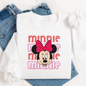 A white t-shirt with a Minnie Mouse design and the text "Minnie" printed on it, along with a red bow on her head.