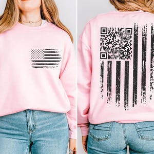 A woman wearing a pink sweatshirt with an American flag design and a QR code on the back.