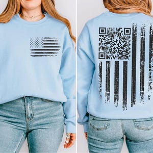 A woman wearing a light blue sweatshirt with an American flag design and a QR code printed on the back.