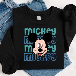 A black t-shirt with a Mickey Mouse graphic printed on it, along with a pair of blue jeans.
