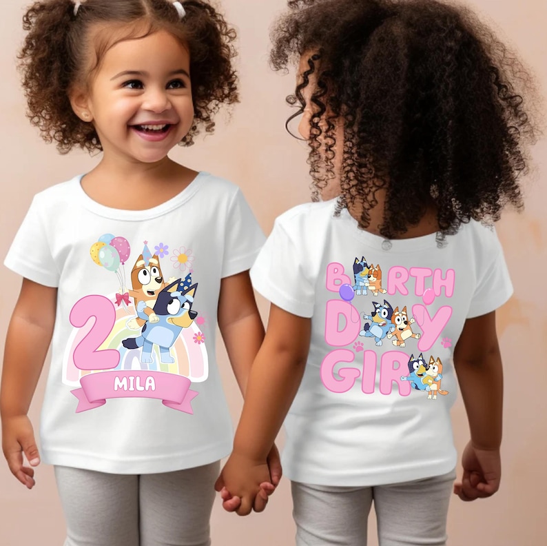 A young girl wearing a white t-shirt with a cartoon character design and the text "2 MILA" printed on it.