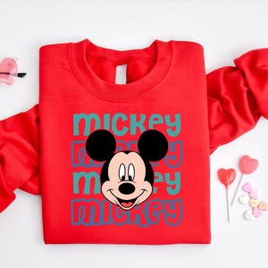 A red sweatshirt with a Mickey Mouse graphic printed on it, along with some heart-shaped candies and a pair of sunglasses.