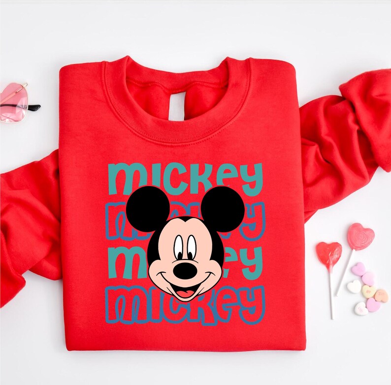A red sweatshirt with a Mickey Mouse graphic printed on it, along with some heart-shaped candies and a pair of sunglasses.