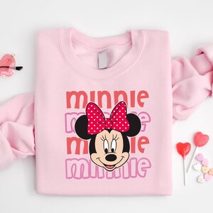 A pink sweatshirt with a Minnie Mouse design and the text "Minnie Minnie" printed on it, along with a bow on her head.
