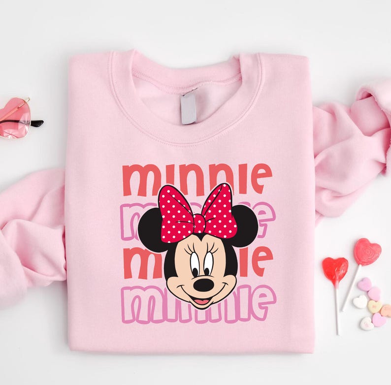 A pink sweatshirt with a Minnie Mouse design and the text "Minnie Minnie" printed on it, along with a bow on her head.