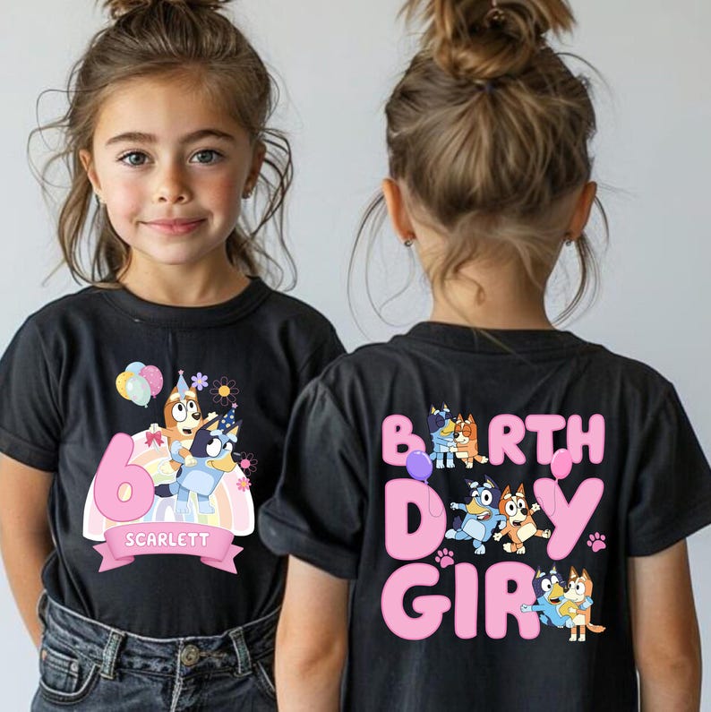 A young girl wearing a black t-shirt with a birthday theme, featuring cartoon characters and the text "6 SCARLET" on the back.