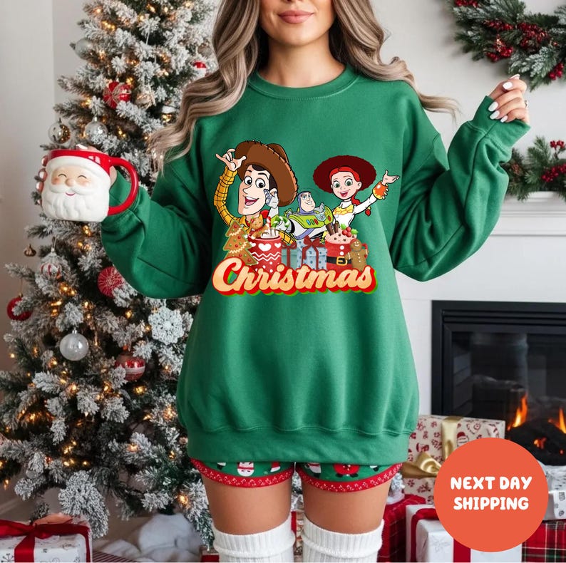 A woman wearing a green sweater with a Christmas-themed design, including characters from the Toy Story movie, is holding a mug in front of a Christmas tree.