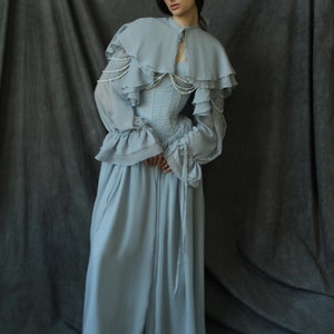 May include: A light blue, flowing, long-sleeved dress with a ruffled cape and a pearl-embellished bodice.