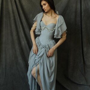 May include: A woman wearing a light blue dress with a ruffled bodice and pearl embellishments. The dress has a fitted bodice and a flowing skirt.