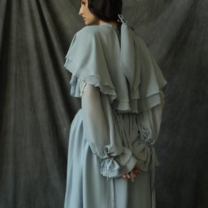May include: A light blue, flowing dress with a ruffled neckline and long sleeves. The dress has a cinched waist and a flowing skirt.
