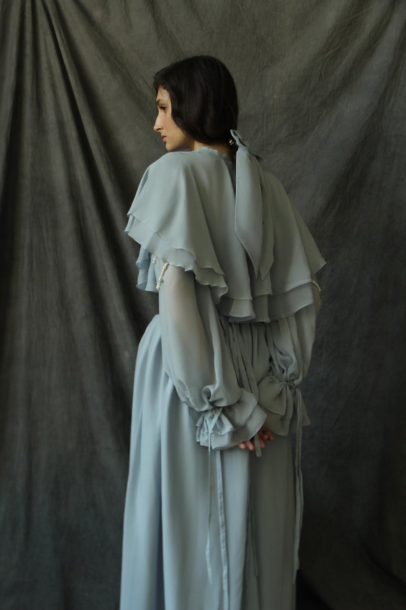 May include: A light blue, flowing dress with a ruffled neckline and long sleeves. The dress has a cinched waist and a flowing skirt.