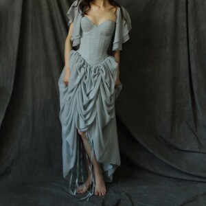 May include: A light blue, floor-length gown with a fitted bodice and a full skirt. The bodice has a sweetheart neckline and is cinched at the waist. The skirt is gathered and has a ruffled hem.