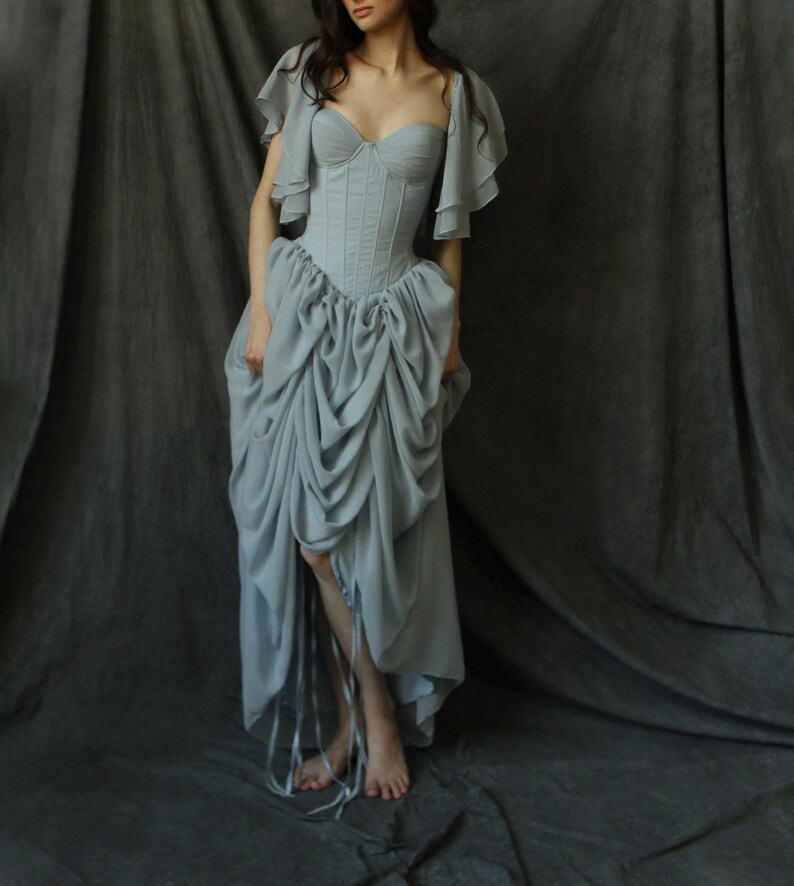 May include: A light blue, floor-length gown with a fitted bodice and a full skirt. The bodice has a sweetheart neckline and is cinched at the waist. The skirt is gathered and has a ruffled hem.