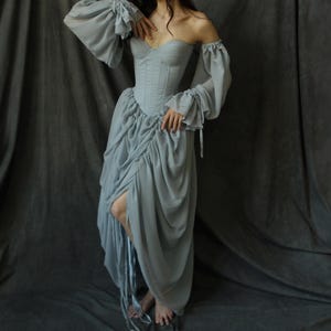 May include: A light blue off-the-shoulder dress with a fitted bodice and a flowing skirt. The dress has a corset-style top with boning and a gathered skirt.