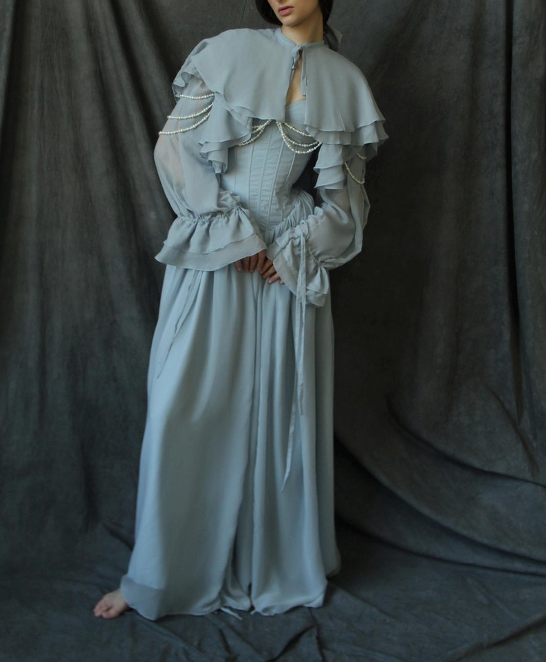 May include: A light blue, flowing, long-sleeved dress with a ruffled cape and a pearl-embellished bodice.