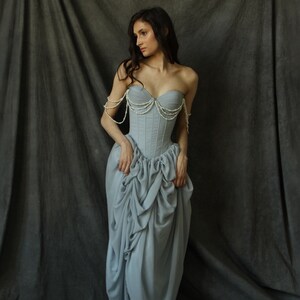 May include: A woman wearing a light blue strapless gown with a pearl-embellished bodice. The gown has a gathered skirt and is styled with a pearl necklace and matching bracelets.