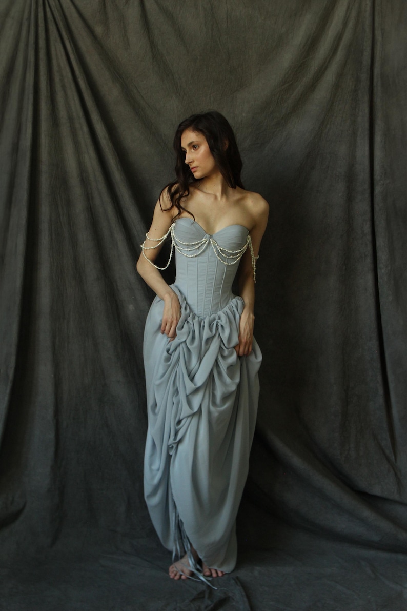 May include: A woman wearing a light blue strapless gown with a pearl-embellished bodice. The gown has a gathered skirt and is styled with a pearl necklace and matching bracelets.