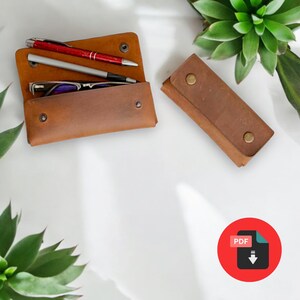 Puede incluir: Dos estuches de cuero marrón, uno con un par de gafas y dos bolígrafos en su interior, el otro vacío. Los estuches están sobre una superficie blanca con plantas verdes en el fondo. La imagen incluye un círculo rojo con la palabra "PDF" y una flecha de descarga.