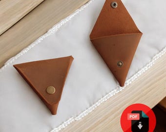 May include: Two brown leather triangle-shaped coin purses with a snap closure. The purses are on a white surface with a crocheted edge.