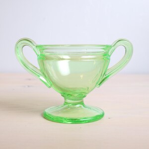 May include: A green glass sugar bowl with two handles and a pedestal base.