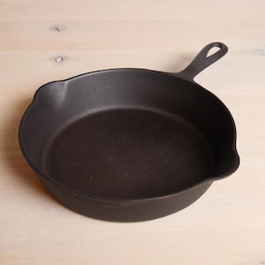 Peut inclure: Une poêle en fonte noire avec une seule poignée. La poêle est vide et a une surface légèrement rugueuse.