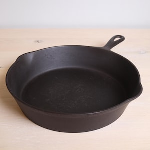 Peut inclure: Une poêle en fonte noire avec une seule poignée. La poêle est vide et a une surface usée et assaisonnée.