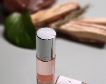 May include: Two small glass bottles with silver caps and labels that say "SAMO" and "Parfum" with a 10 ml measurement. The bottles are on a light gray surface.