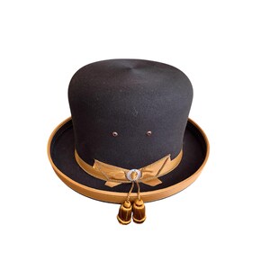 May include: A black felt fedora hat with a brown leather band and gold trim. The hat has two tassels hanging from the band.