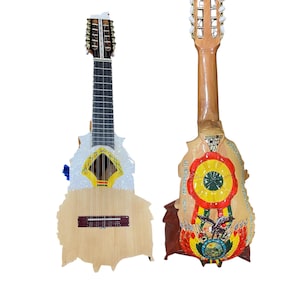 Könnte beinhalten: Zwei Charangos, traditionelle Anden-Saiteninstrumente, werden gezeigt. Die Charangos haben helle Holzkörper, Griffbretter und mehrere Saiten. Eines hat ein weißes und gelbes Design, das andere ein farbenfrohes Emblem.