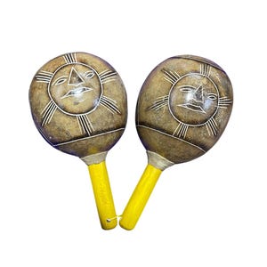 May include: Two handcrafted maracas with a sun face design carved into the brown gourd bodies. The handles are painted yellow. These musical instruments are ideal for percussion and music enthusiasts.