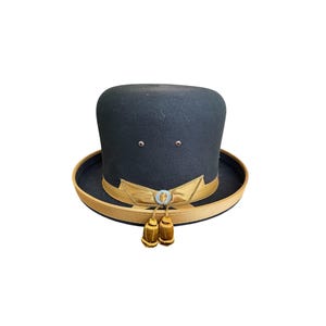 May include: A black felt top hat with a gold band and tassels. The hat has a small circular emblem with a design on it.