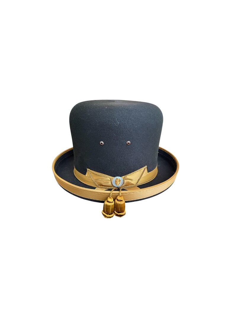 May include: A black felt top hat with a gold band and tassels. The hat has a small circular emblem with a design on it.