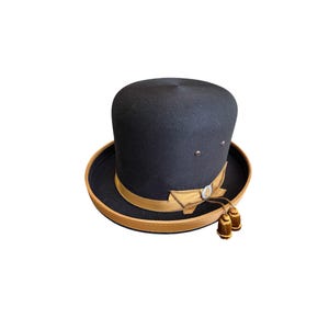 May include: A black felt top hat with a brown leather band and a gold bow. The hat has two small gold tassels.