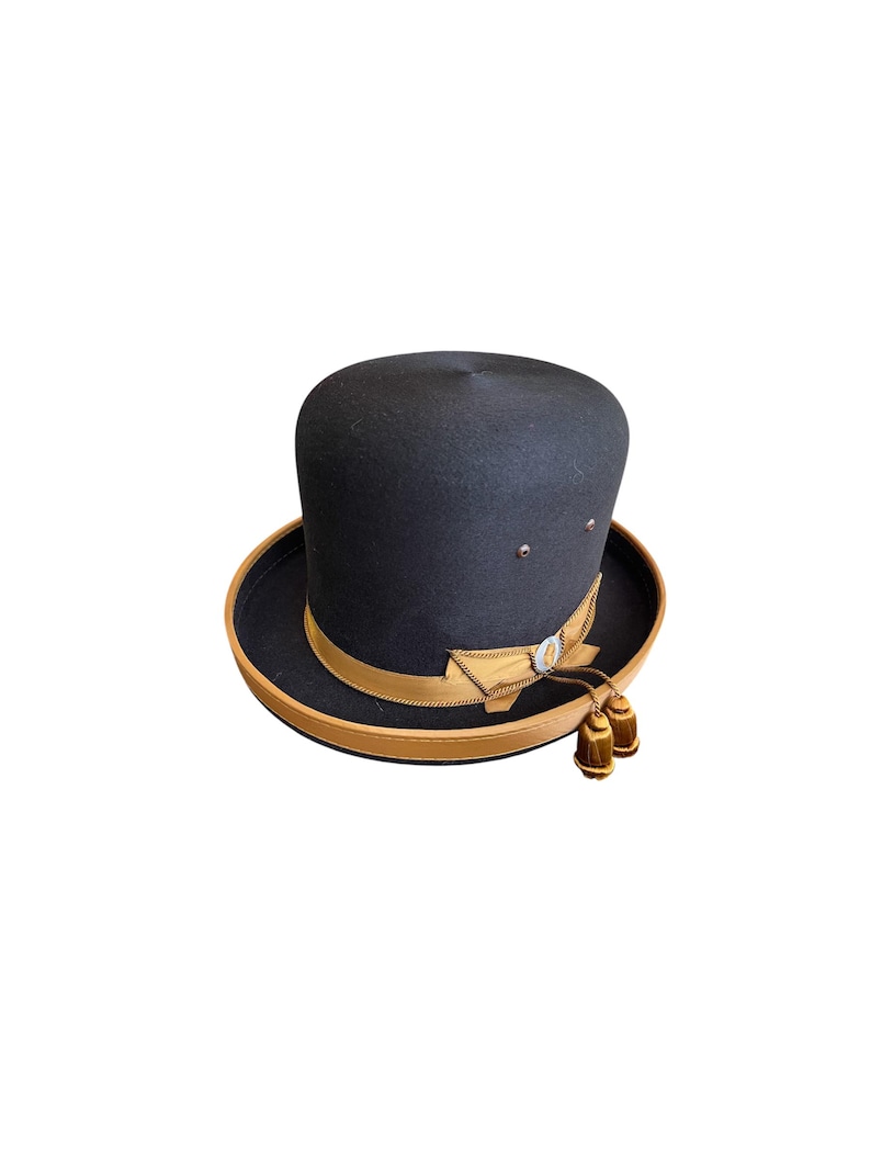 May include: A black felt top hat with a brown leather band and a gold bow. The hat has two small gold tassels.