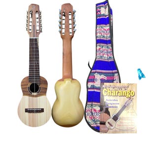 May include: Two charangos, small stringed instruments, are displayed, one with a light wood body and the other with a darker wood body. A blue and patterned case and a book titled "Charango" are also present. The instruments are designed for playing music.