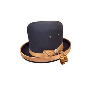 May include: A black felt fedora hat with a brown ribbon and two gold tassels. The hat has a small silver button on the front.