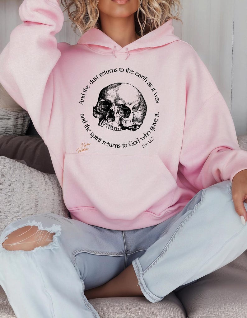 May include: A light pink hoodie with a black and white skull graphic. The graphic is surrounded by text that reads "And the dust returns to the earth as it was, and the spirit returns to God who gave it. Ecc 12:7."