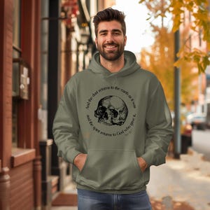 May include: An olive green hoodie with a front pocket and a drawstring hood. The hoodie features a black skull graphic with the text "And the dust returns to the earth as it was and the spirit returns to God who gave it."