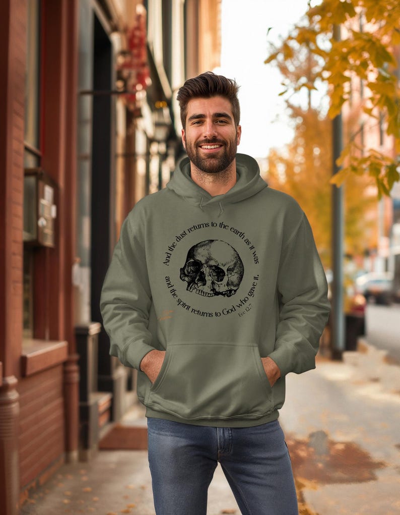 May include: An olive green hoodie with a front pocket and a drawstring hood. The hoodie features a black skull graphic with the text "And the dust returns to the earth as it was and the spirit returns to God who gave it."