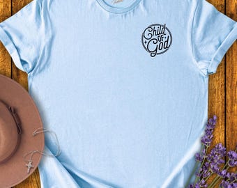 May include: A light blue t-shirt with a black circle design that says "Child of God" in a vintage font.