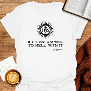 Puede incluir: Camiseta blanca con un gráfico en blanco y negro de un sol con las letras IHS en su interior. El texto debajo dice "IF IT'S JUST A SYMBOL TO HELL WITH IT F O'Connor".