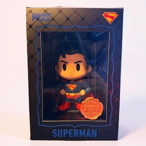 May include: A Superman collectible figure in a black box with a clear window. The box features the text PIX!, SUPERMAN, and a red and yellow shield logo. Inside, the figure wears a blue suit with a red cape and emblem. An orange seal reads LIMITED EDITION 9999 PCS.