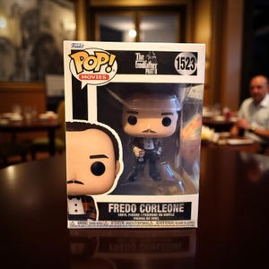 May include: A Funko Pop! vinyl figure of Fredo Corleone from The Godfather Part II. The figure is in a clear plastic display case. The box features the Funko Pop! Movies logo and the number 1523.
