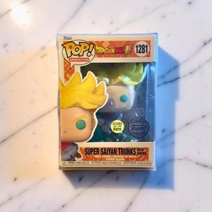 May include: A Funko Pop! Animation figure of Super Saiyan Trunks with a sword. The figure has yellow hair and is in a clear plastic display case. The box has the Dragon Ball Z logo and the number 1281.