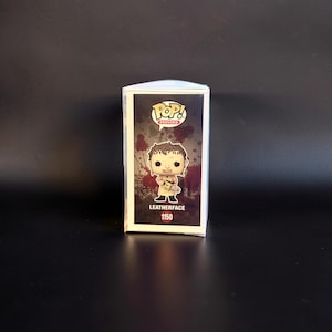 May include: A Funko Pop Movies vinyl figure of Leatherface, number 1150, inside its original rectangular packaging. The box features a graphic of the character holding a chainsaw against a dark, blood-splattered background with the Pop logo.