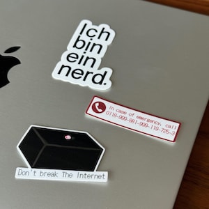 Puede incluir: Una colección de pegatinas en un portátil. Una pegatina dice "Ich bin ein nerd." Otra dice "In case of emergency, call 0118-999-881-999-119-725-3." Una tercera pegatina dice "Don't break The Internet."