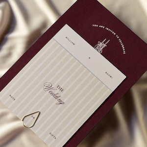 May include: A wedding invitation suite featuring a burgundy card with the text "YOU ARE INVITED TO CELEBRATE". The invitation card has a cream and white striped pattern with the words "THE Wedding" and the names "William & Naomi". A gold paper clip is attached.