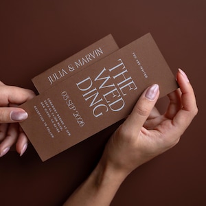 Puede incluir: Tarjetas de invitación de boda marrones con texto blanco. Las tarjetas dicen "THE WEDDING" e incluyen la fecha "03 SEP 2026". Los nombres "JULIA & MARVIN" también están impresos en las tarjetas. Las tarjetas están en las manos de una persona.