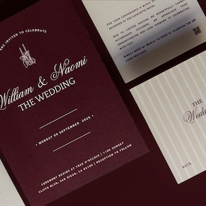 May include: Burgundy wedding invitation suite with white calligraphy. The main invitation reads "William & Naomi THE WEDDING" with the date and location. Additional cards include RSVP information and a note card. Elegant design.
